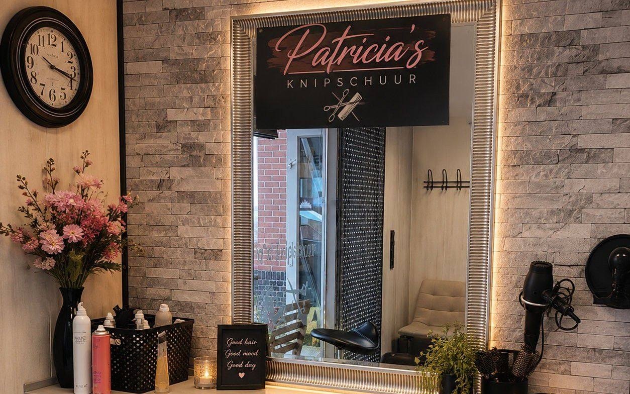 Een werkplek in de salon: de spiegel met het verlichte naambord Patricia's Knipschuur, bloemen en kaarsjes